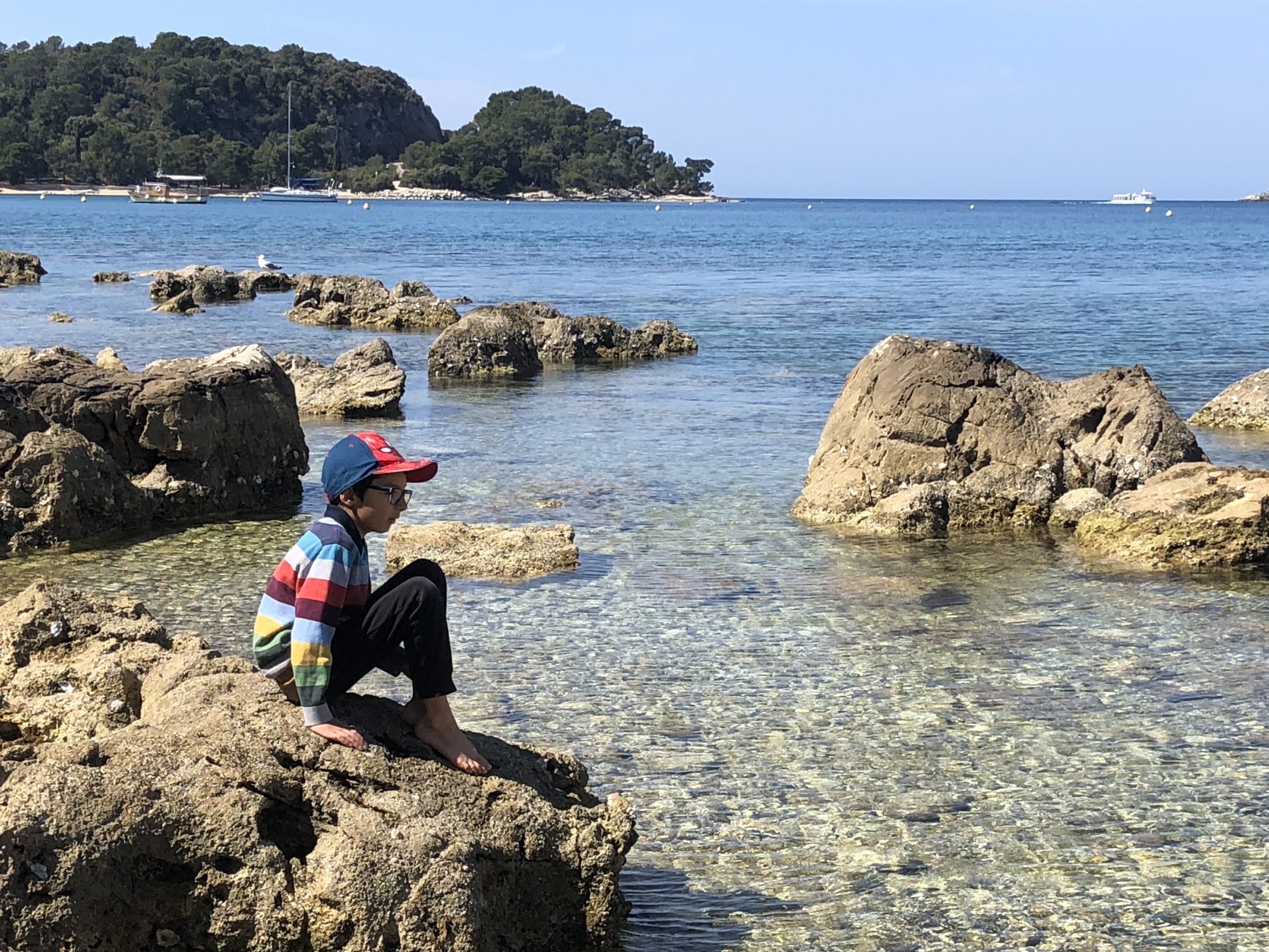 Boy by the sea with clear water and rocks