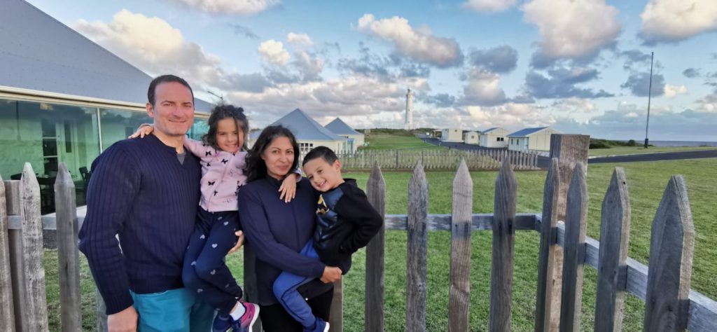 Family posing in front of a wooden barrier with sky and clouds behind