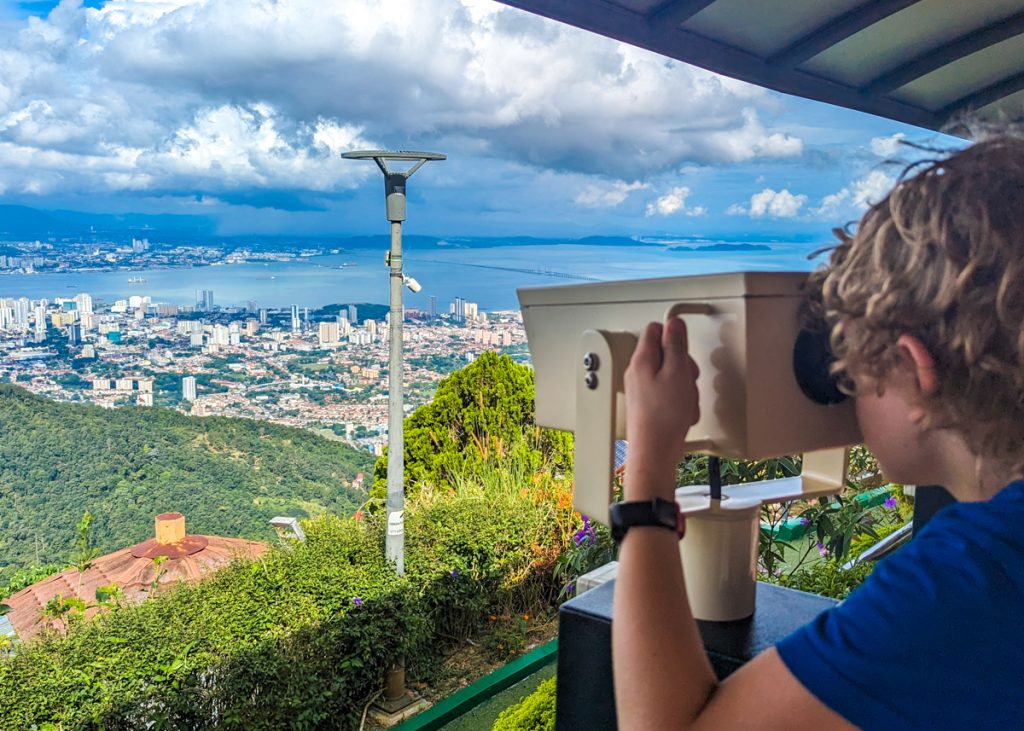 Child looking through binoculars over a city and sea