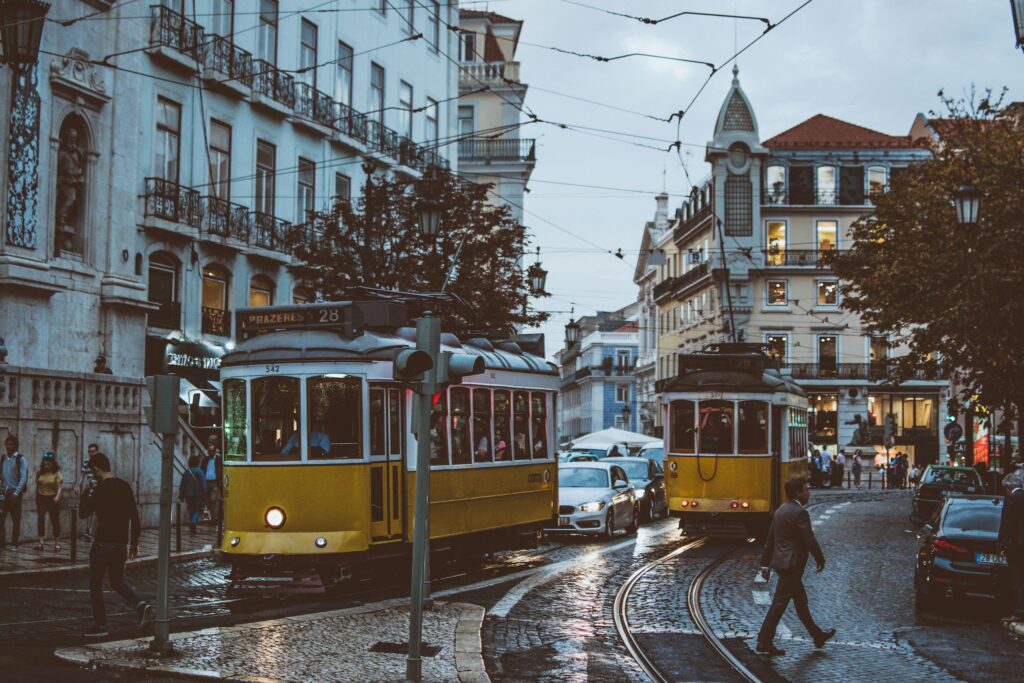 Yellow and White trams in a street with cars and pedestrian.