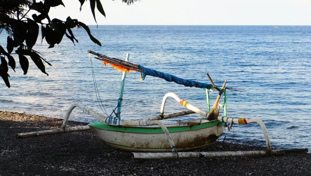 A traditional fishing boat rests on a pebble beach in Amed, Bali, overlooking the calm ocean waters.